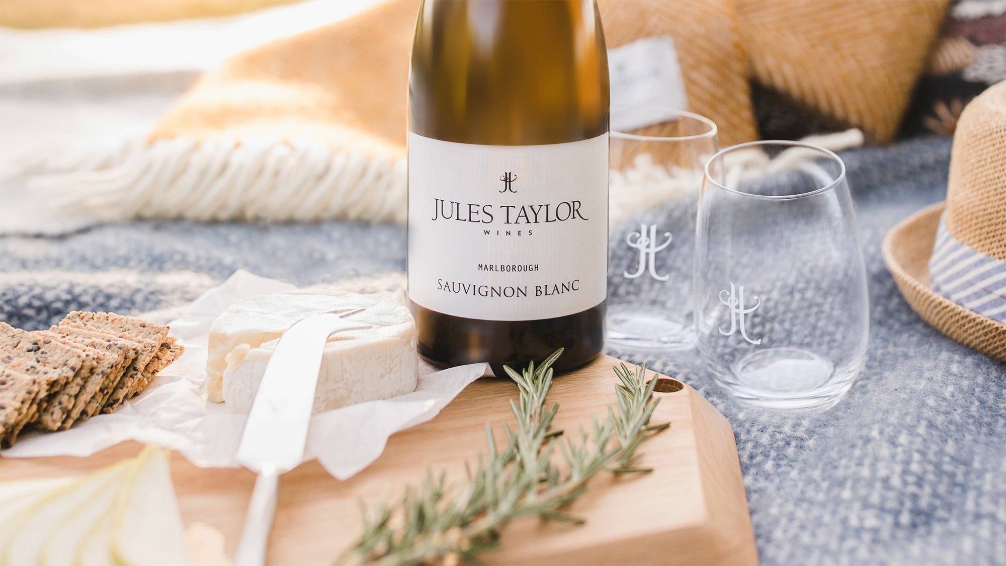 Jules Taylor Sauvignon Blanc wine bottle on a wooden board with cheese and crackers, outdoor setting.