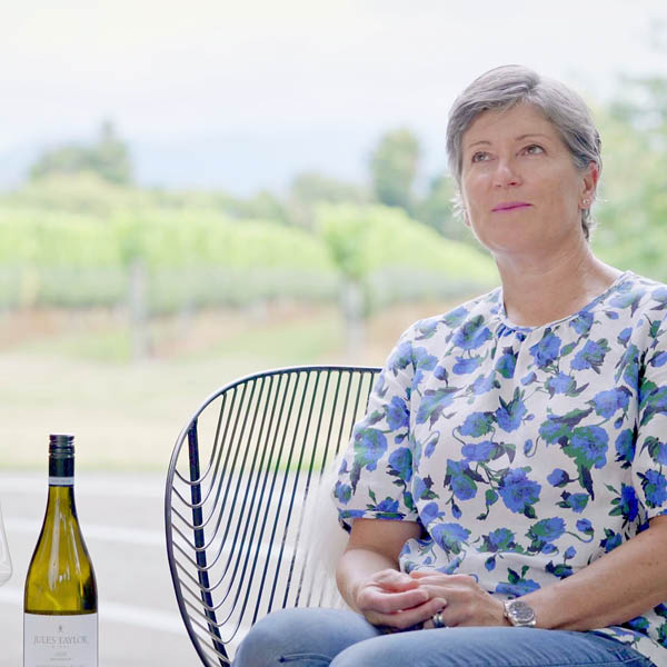 Jules Taylor sitting outdoors with a bottle of wine, surrounded by greenery